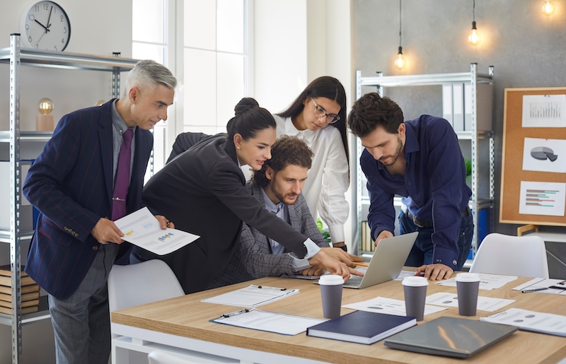 Colleagues discuss a business project by comparing analysis data and graphs on a laptop.